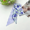 Un foulard en soie floral violet et blanc est exposé à côté d'un bol de pommes vertes et d'une bouteille.