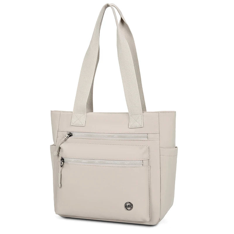 A beige canvas tote bag with two zippered pockets and padded handles.