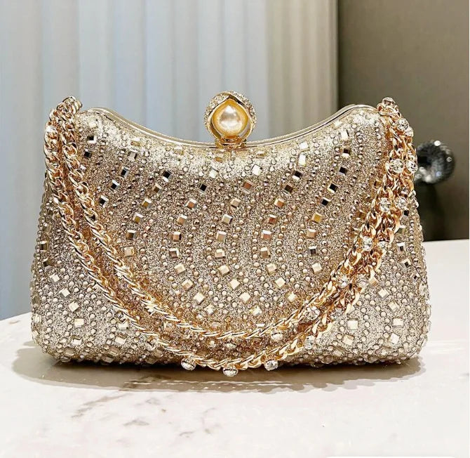 A sparkling gold and diamond rhinestone clutch bag with a pearl closure resting on a white surface.