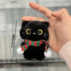 Una mano sostiene un llavero colgante de un peluche de gato negro, mostrando su tamaño y detalle.
