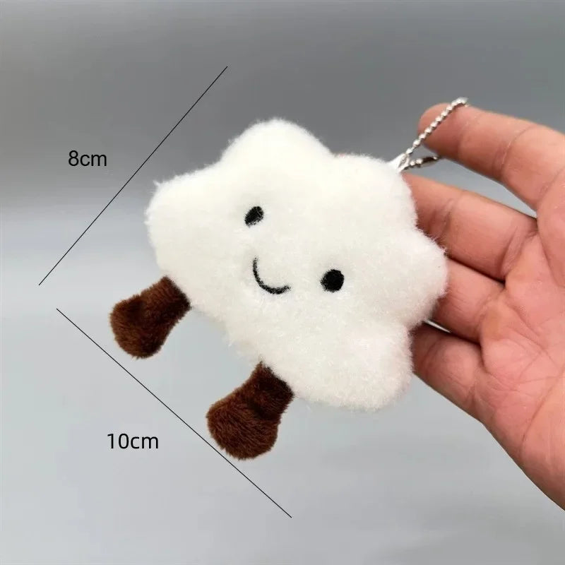 A white fluffy cloud shaped plush pendant keychain with brown accents is held in a hand.