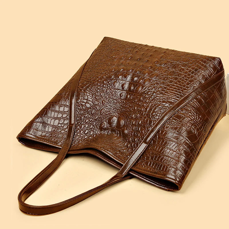 A brown crocodile print leather tote bag with a strap is shown on a light background.