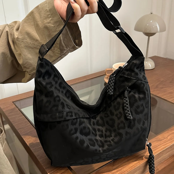 Eine schwarze Leopardenmuster-Crossbodytasche wird von einer Hand gehalten und liegt auf einer Holzoberfläche.
