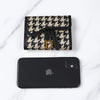 Portefeuille avec motif houndstooth noir et blanc à côté d'un smartphone noir.