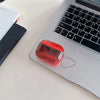 A clear red luminous sand effect earphone case resting on a silver laptop keyboard.
