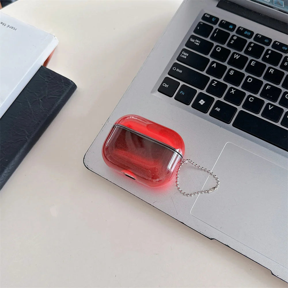 A clear red silicone earphone case with a silver chain is placed on a laptop keyboard.