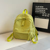 A lime green corduroy daily backpack is displayed on a white surface next to a framed poster.