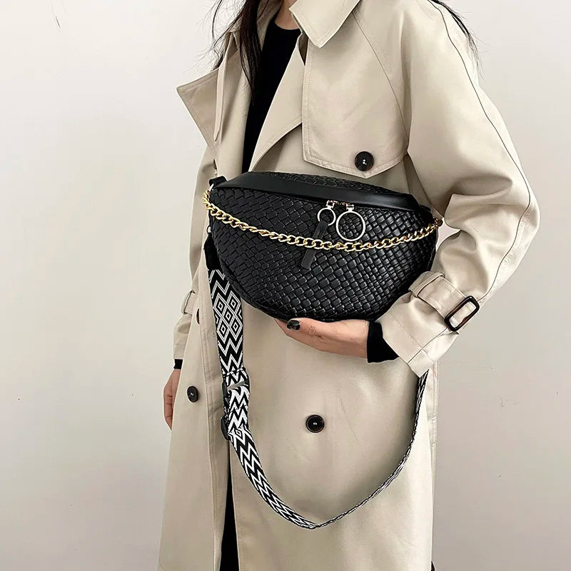 A beige trench coat features a black woven pattern waist bag with gold chain detailing and a patterned strap.