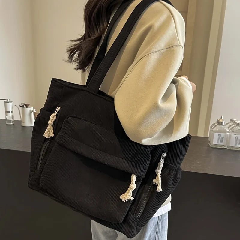 Un sac fourre-tout en velours côtelé noir à multiples poches est porté par une personne.