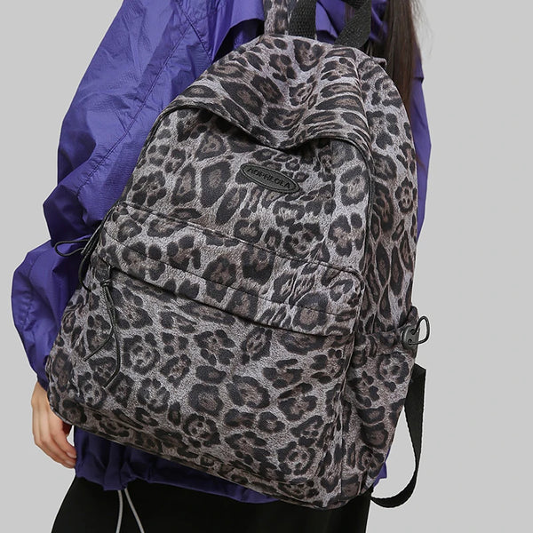 A woman is holding a leopard print women's backpack in purple clothing.