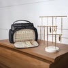 A black multi-compartment travel organizer bag with a light beige interior and jewelry display rack on a wooden surface.