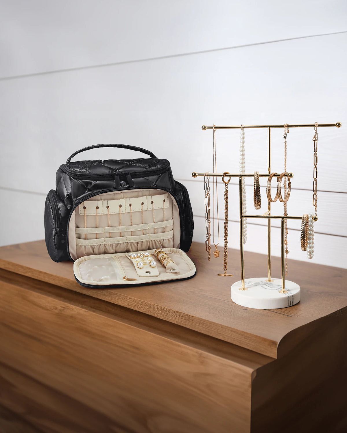 A black multi-compartment travel organizer bag with a light beige interior and jewelry display rack on a wooden surface.