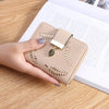 Una mano sostiene un bolso cartera de cuero sintético beige con un colgante dorado sobre una mesa de madera.