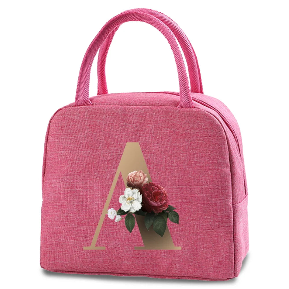 A pink insulated canvas lunch bag featuring a gold letter A design with a small floral arrangement.