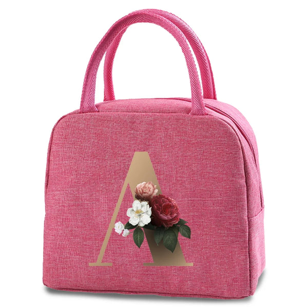 A pink insulated canvas lunch bag featuring a gold letter A design with a small floral arrangement.
