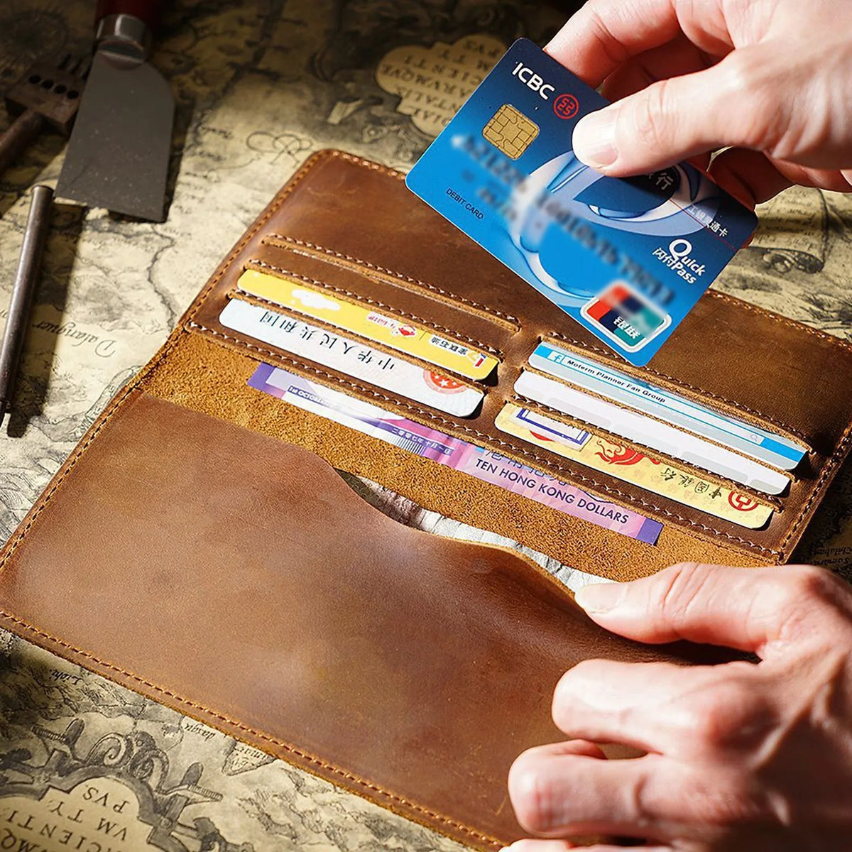 A hand is holding an ICBC debit card and several other cards inside a brown leather long bi-fold wallet.
