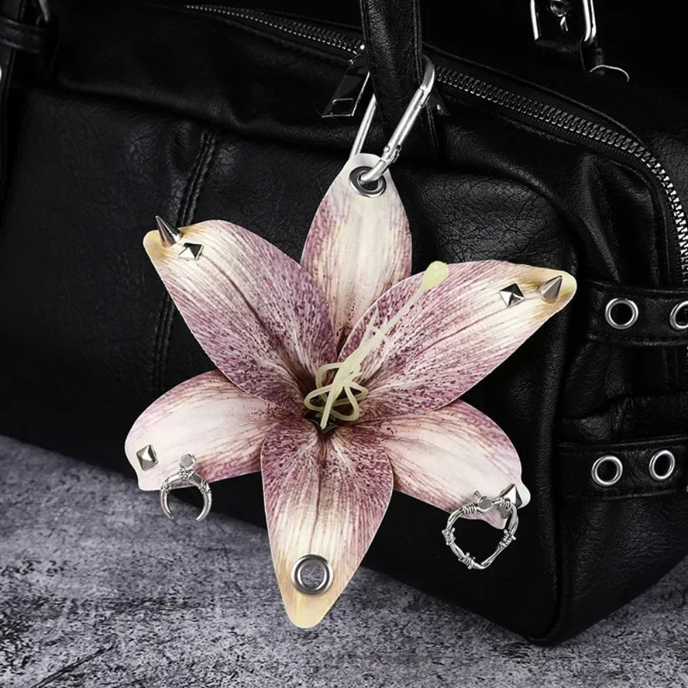 A realistic orchid flower keychain with purple and white markings hangs from a black leather bag.