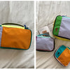 Two waterproof travel toiletry bags in purple, orange, and lime green nylon construction lying on a white sheet.