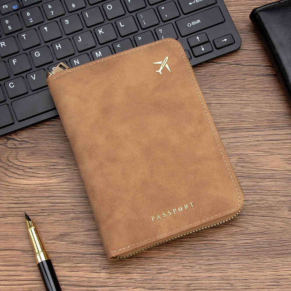 A brown passport wallet with a gold-toned zipper and a silver logo rests on a wooden desk next to a black laptop keyboard.