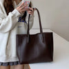 A woman holds a dark brown leather tote bag with handles against a white background.