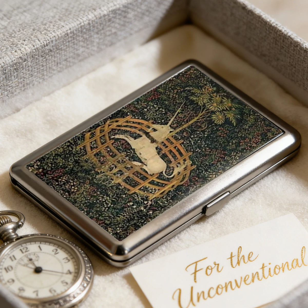 An Art Deco metal card holder with a dark green patterned surface resting in a light-colored box.