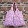 A pink and white patterned reusable shopping bag hanging against a brick wall.