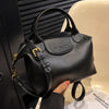 A black vintage PU leather crossbody handbag is held in a hand next to a white sink.