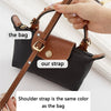 A hand holds a black leather crossbody bag with a brown leather strap, showing the bag and strap details.