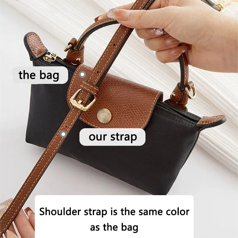 A hand holds a black leather crossbody bag with a brown leather strap, showing the bag and strap details.