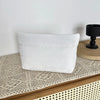 A white quilted cosmetic travel bag resting on a woven mat.
