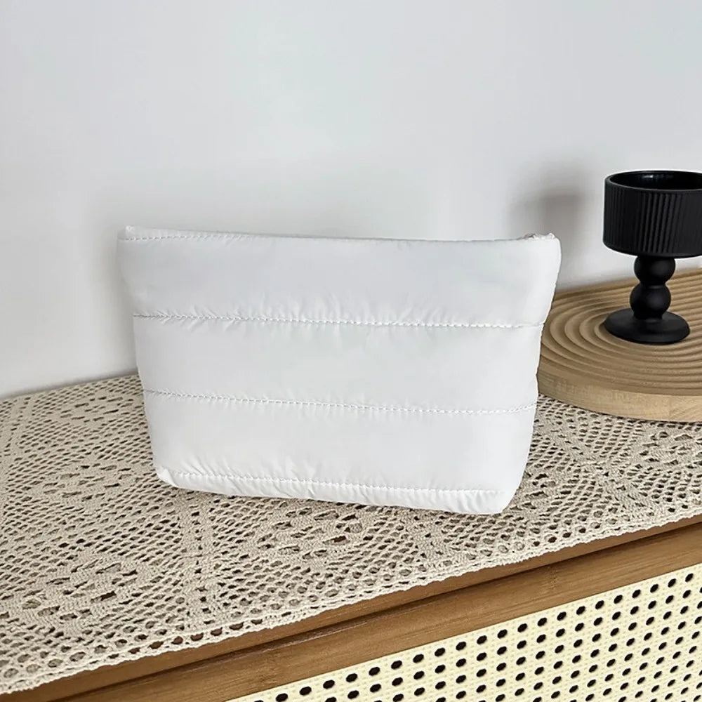 A white quilted cosmetic travel bag resting on a woven mat.