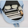 A light blue durable nylon commuter backpack is open, showing a laptop, notebooks, and headphones inside.