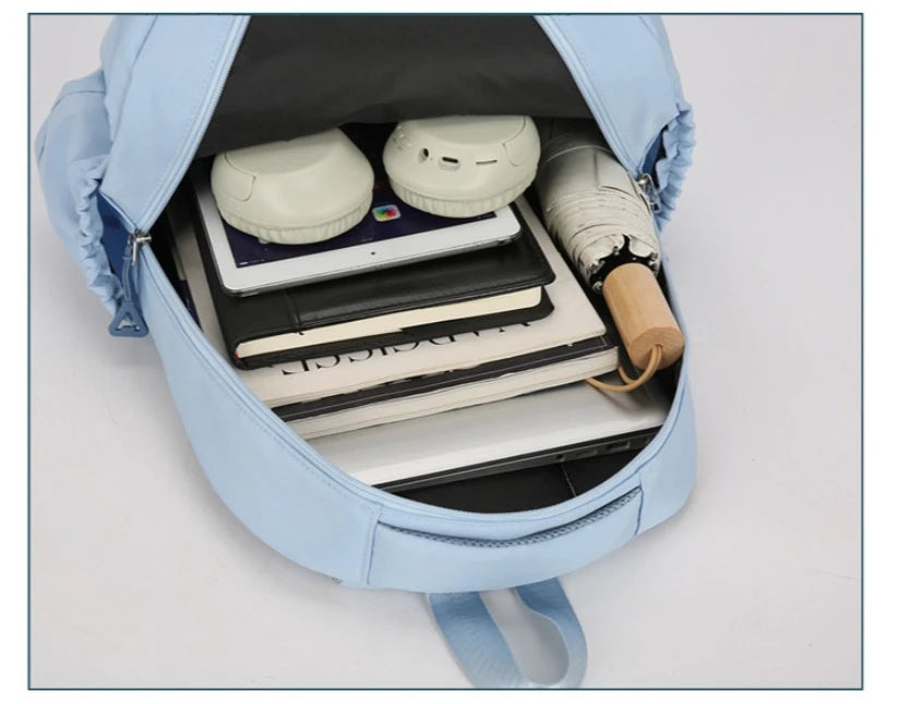 A light blue durable nylon commuter backpack is open, showing a laptop, notebooks, and headphones inside.