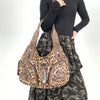 A brown leopard print crossbody shoulder bag worn by a person, set against a light background.