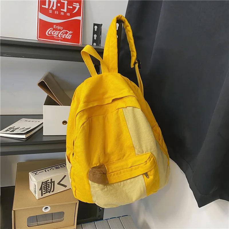 A bright yellow canvas fashion backpack with a tan accent, hanging on a shelf.