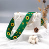 A white quilted crossbody bag with a green sunflower pattern strap and gold hardware resting on a white fabric.