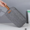 A gray fabric pouch with a brown strap is being held by a hand, shown against a light background.
