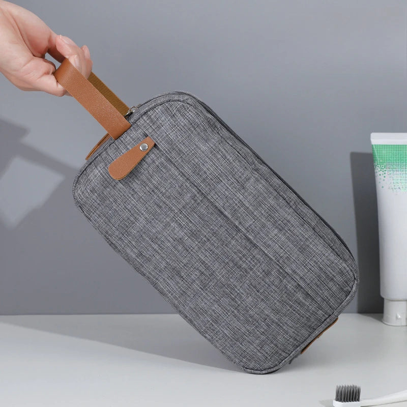 A gray fabric pouch with a brown strap is being held by a hand, shown against a light background.
