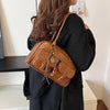 A woman is holding a brown vintage letter print crossbody bag against a black outfit.