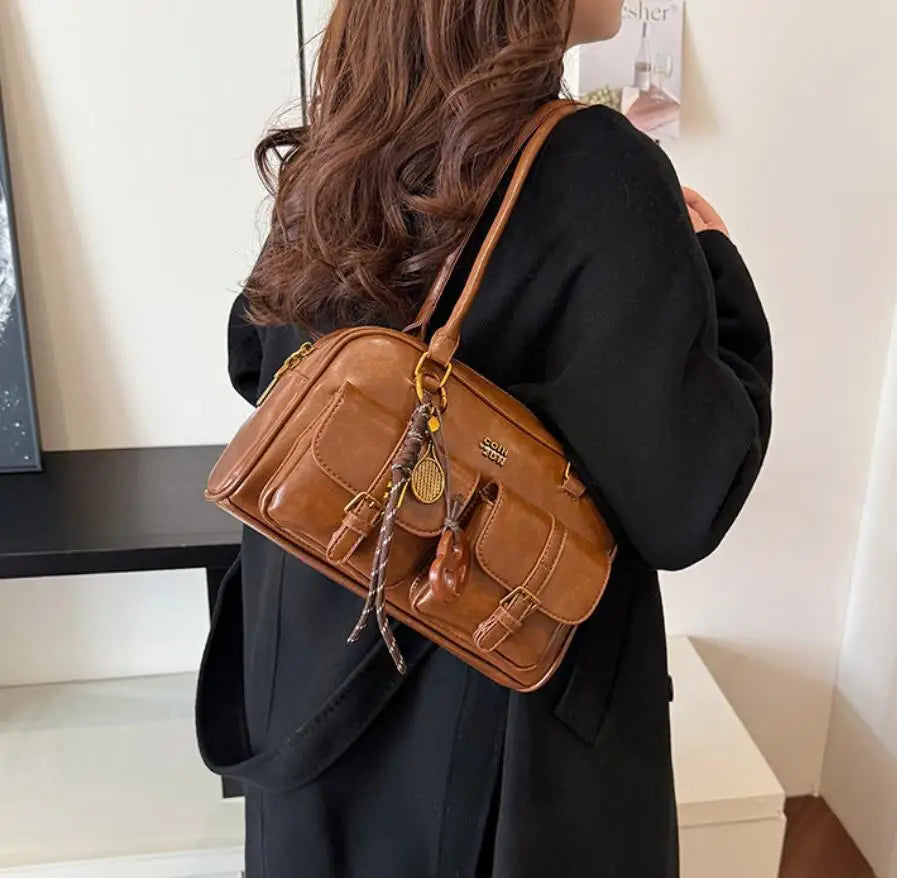 A woman is holding a brown vintage letter print crossbody bag against a black outfit.