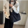 A person is holding a black corduroy multi-pocket tote bag over a cream-colored sweatshirt.