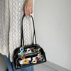 A black handbag with a multi-color acrylic chain strap is held by a person wearing a cream knit sweater.
