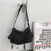 Bolso cruz de lona negra colgado en una puerta, con un gancho plateado visible.