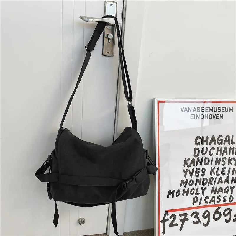 Bolso cruz de lona negra colgado en una puerta, con un gancho plateado visible.