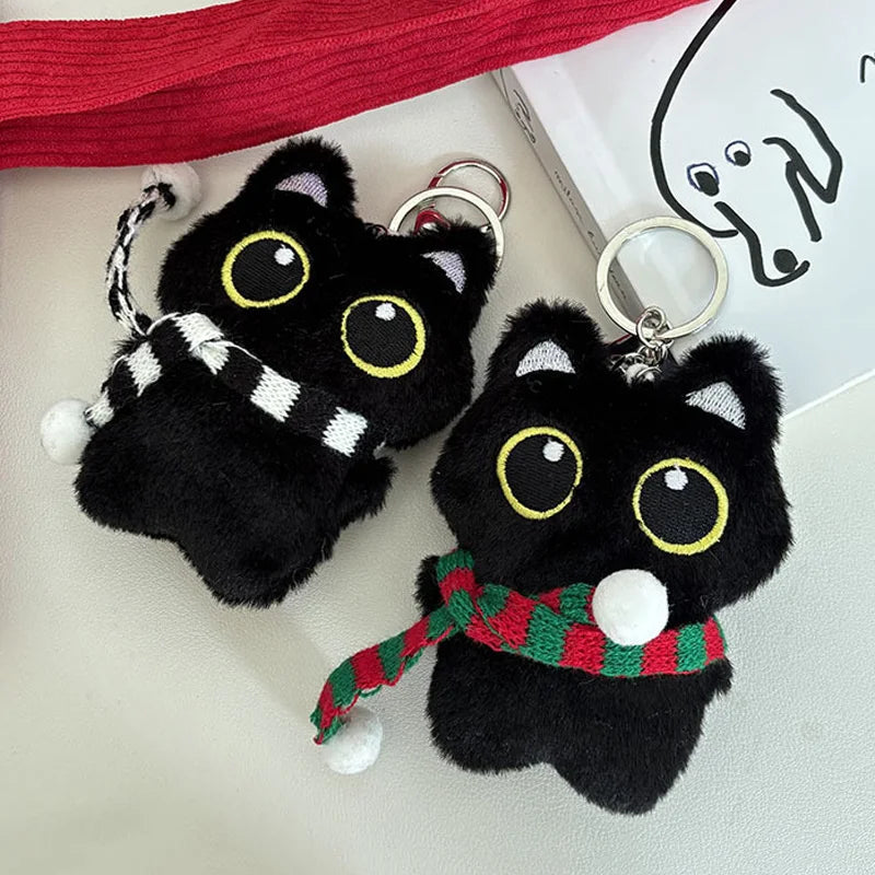 Colgante de llavero de peluche de gato negro con accesorio de rayas blancas y negras en una cinta roja.