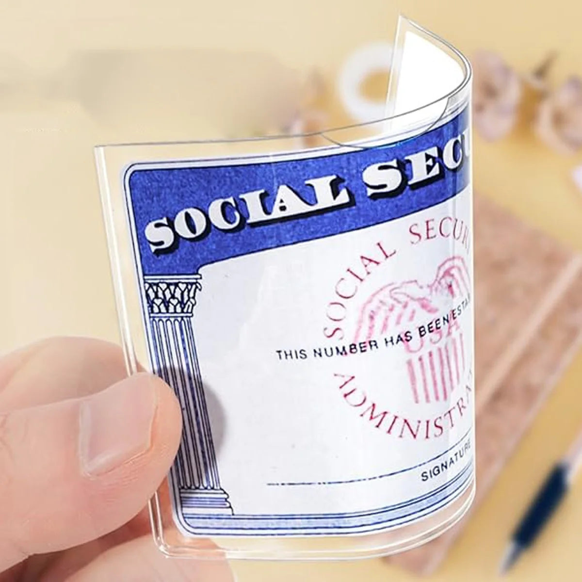 A hand holds a clear PVC card and ID sleeve featuring the Social Security Administration logo and text.