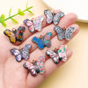 A hand holds a set of colorful butterfly enamel charms in various shades and patterns.