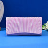 A lavender satin evening clutch with vertical pleats and a chain strap displayed on a blue surface.