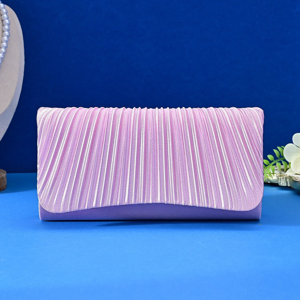 A lavender satin evening clutch with vertical pleats and a chain strap displayed on a blue surface.
