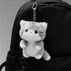 A grey soft cat plush pendant ornament hanging from a keychain on a black backpack.